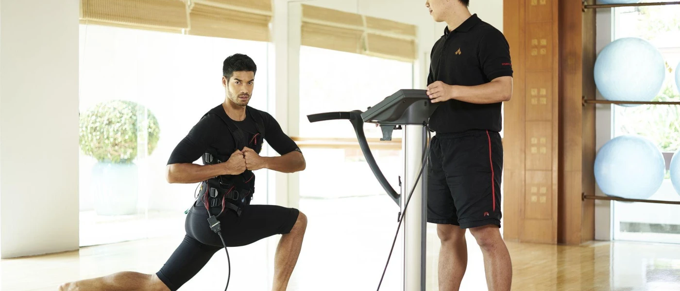 A man in active wear lunges while attached to wires while an expert reads the results from a machine next to him
