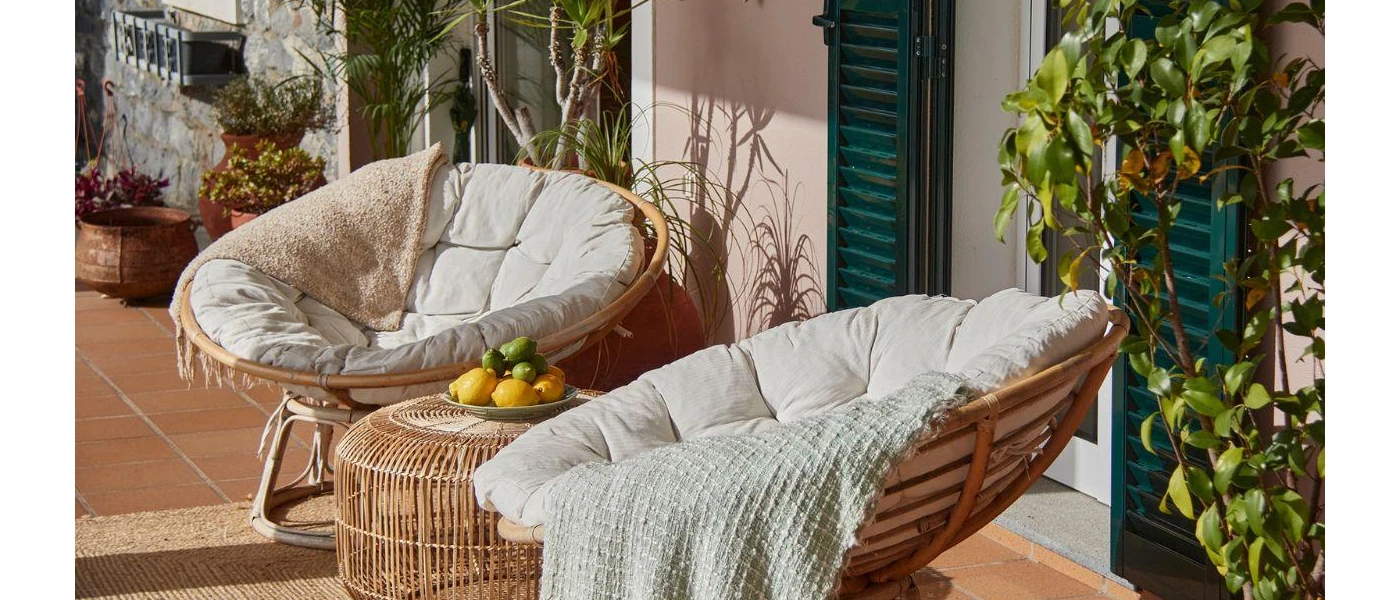 Two rattan chairs and a coffee table with cushions and throws on an outdoor terrace