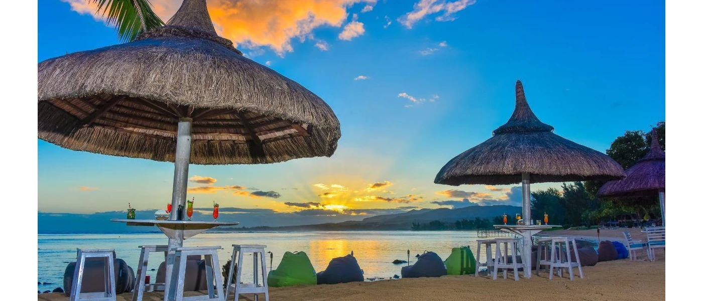 Beachfront bar on the sands, with thatched umbrellas, white wooden chairs and blue and green bean bags at sunset