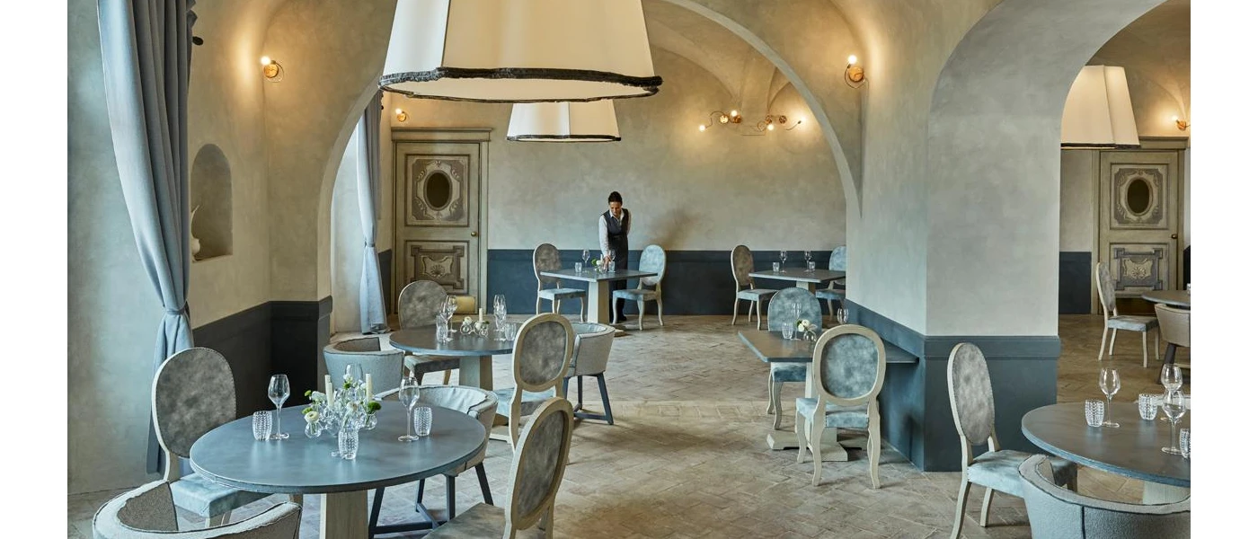 Restaurant with swooping archways and slate tables in grey tones, with a waiter setting up for the next meal