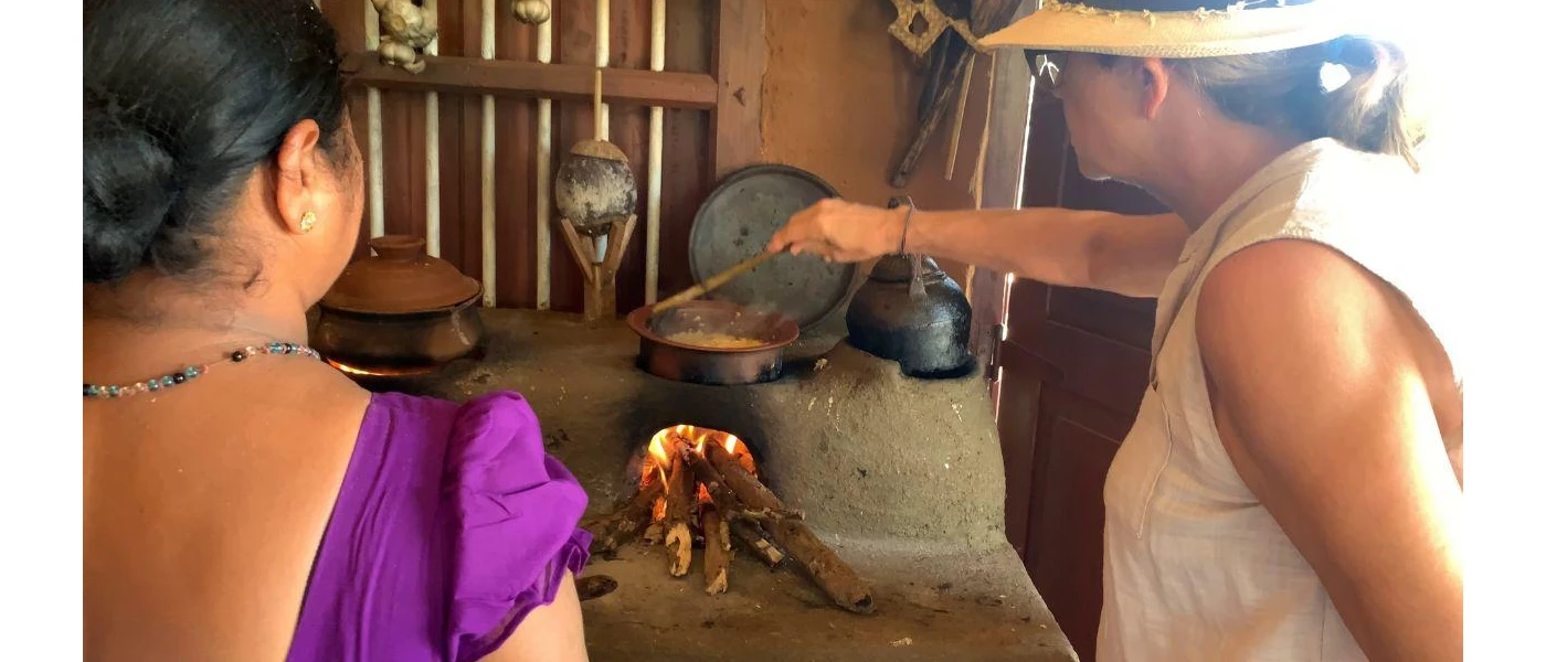 Two women standing over traditional pots on a fire, stirring some food