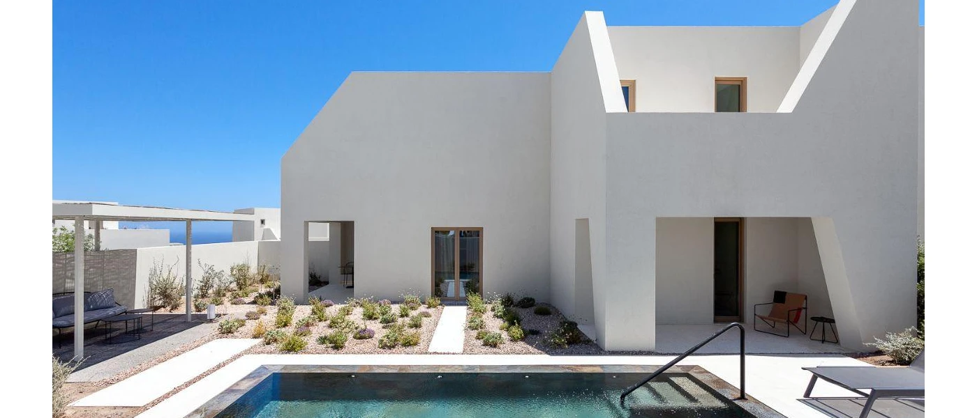 Low-rise white villa under a sunny blue sky with a terrace with planted shrubs and a swimming pool