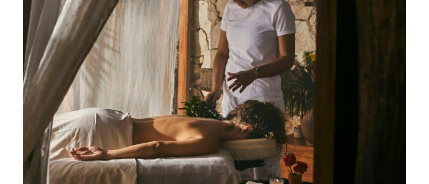 Woman lies on her front in a white towel as a male therapist prepares to massage her back