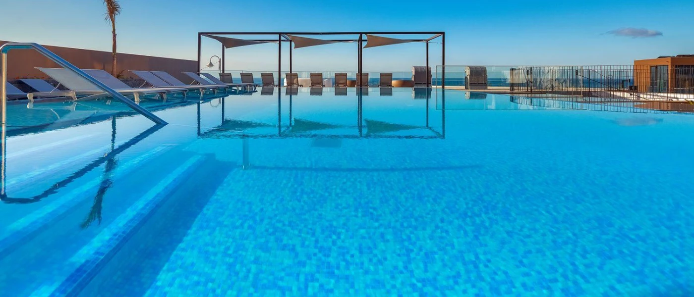 Swimming pool surrounded by loungers overlooking the sea in the distance