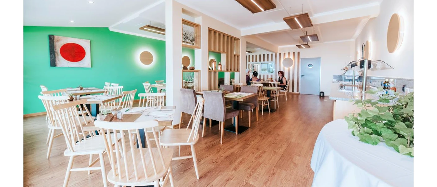 Airy restaurant with blue walls, a wooden floor, tables and chairs and a buffet station to the right-hand side