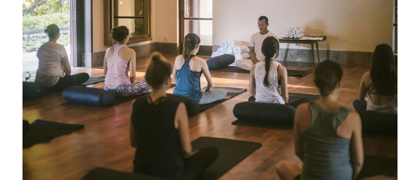 Group sitting on yoga mats in active wear as an instructor leads the class