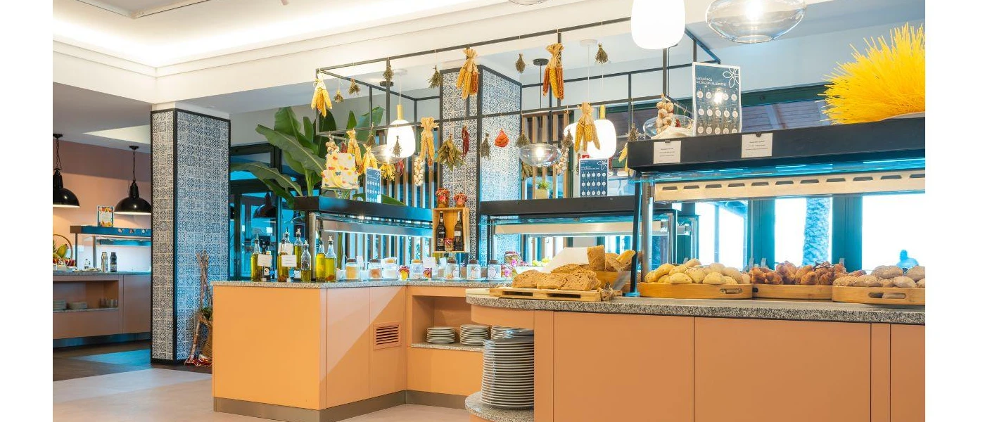 Buffet restaurant laid up for breakfast with baskets of bread and pastries, stacked plates and bottles of olive oil