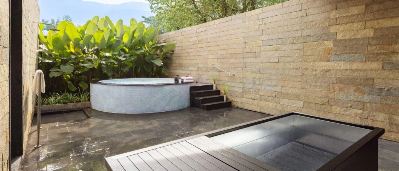 Stone-walled courtyard with tropical shrubs, a bath and steps into a hot tub
