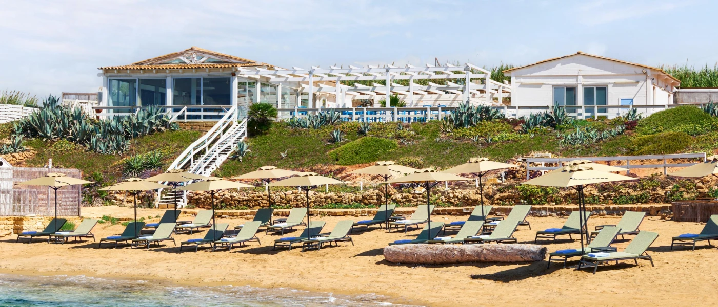 Rustic white terracotta-roofed beach club with steps down to a golden sandy beach with cream loungers and sunbeds