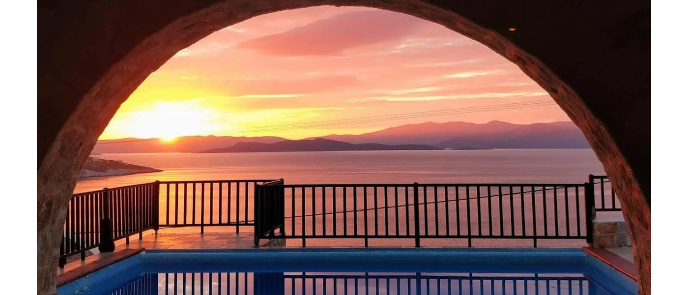 Sun setting over the hills beyond the sea, as seen from the corner of a swimming pool 