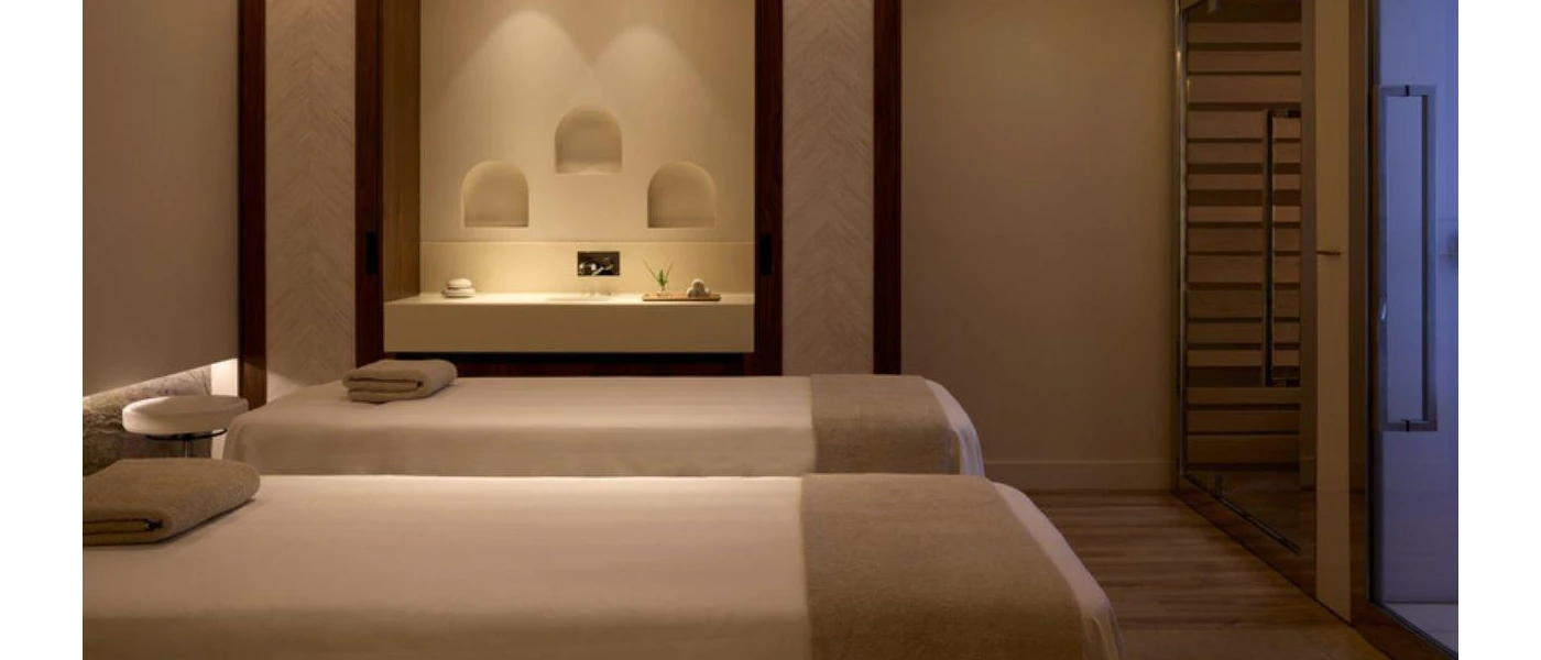 Neutral treatment cabin with two massage beds, a marble vanity unit and soft lighting