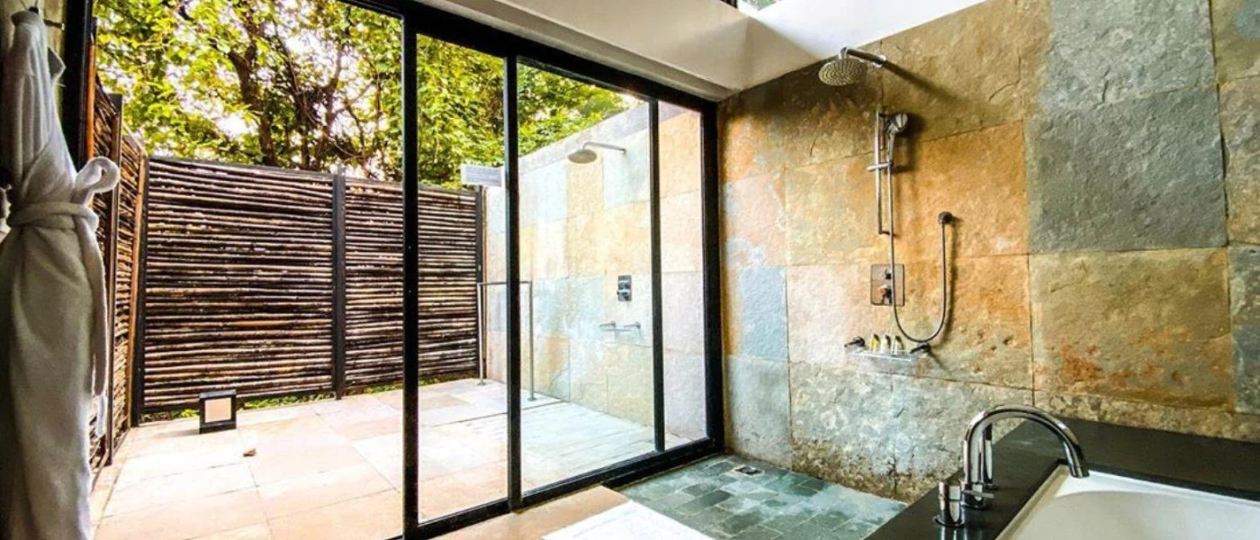 Stone-walled bathroom with a bath, shower and windows to an outdoor courtyard with a shower