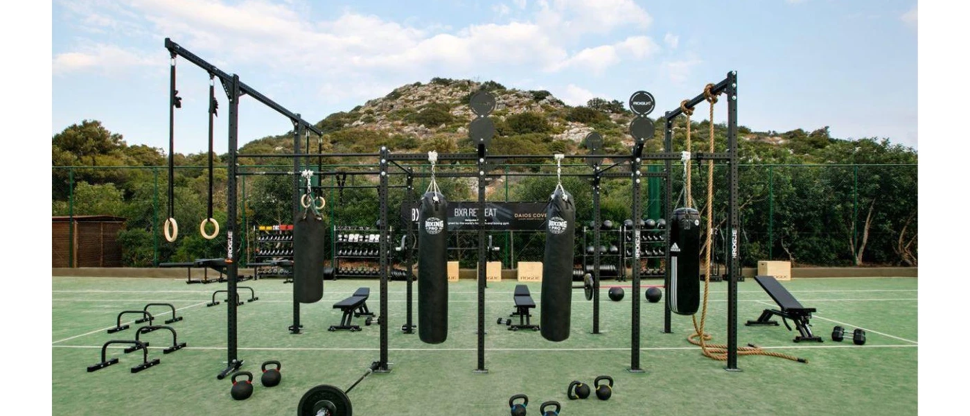 Outdoor gym on astro-turf with a hillside view, with black punch bags, weights and benches