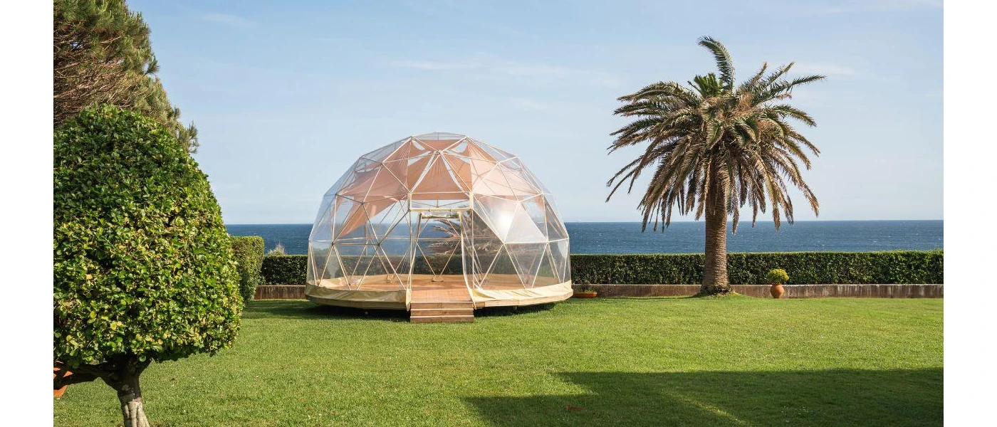 Transparent dome for yoga in a sunny lawned garden with ocean views