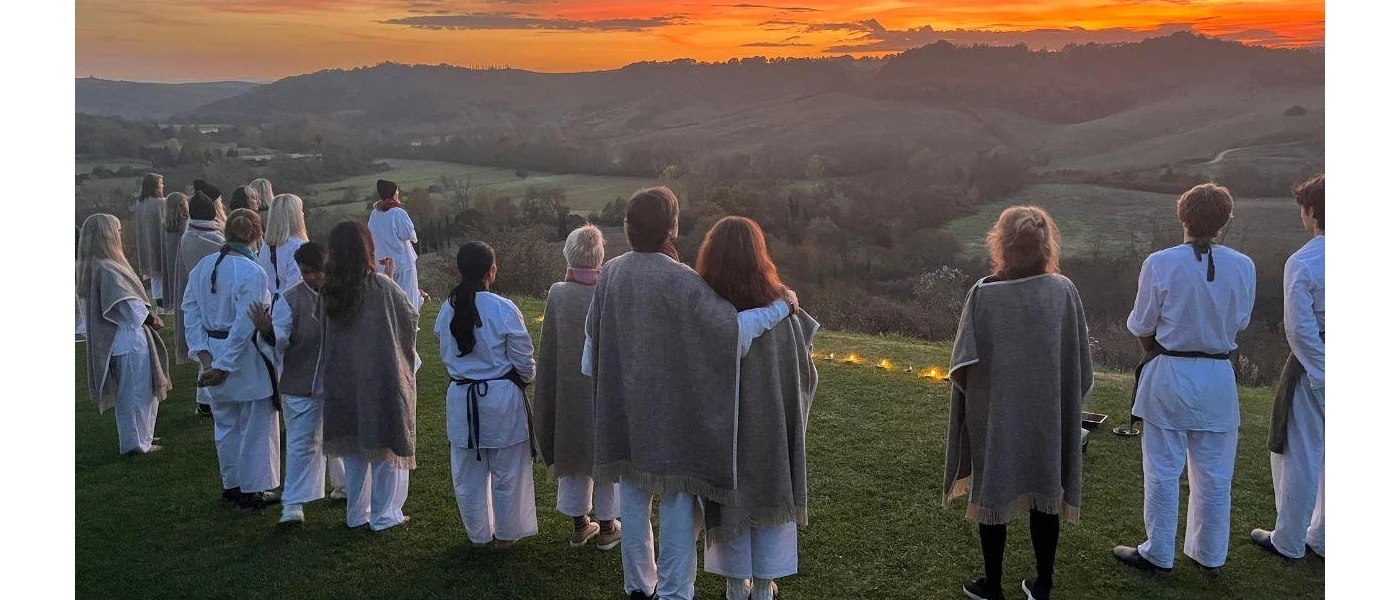 Group stands on a hillside as the sun sets over the mountains in the distance