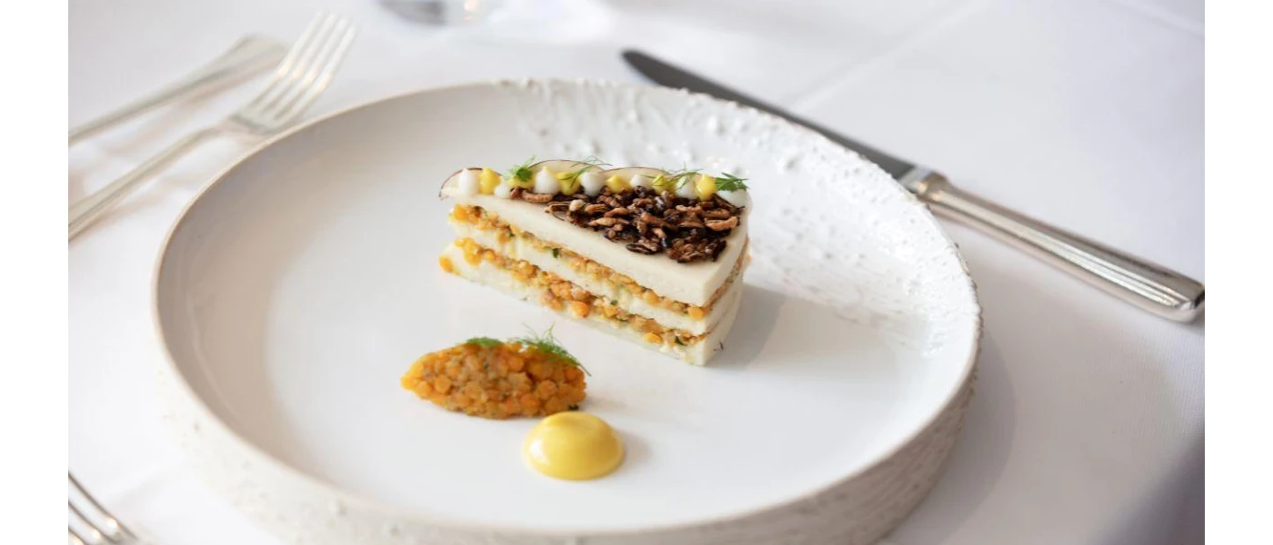 Stacked slice topped with seeds and accompanied by a dollop of sauce on a white plate 