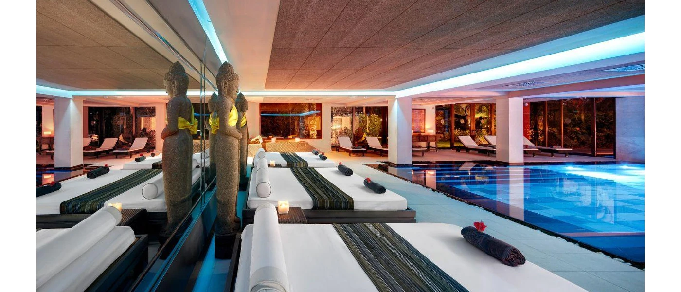 Indoor pool surrounded by white daybeds, Buddha statues and LED ceiling lights