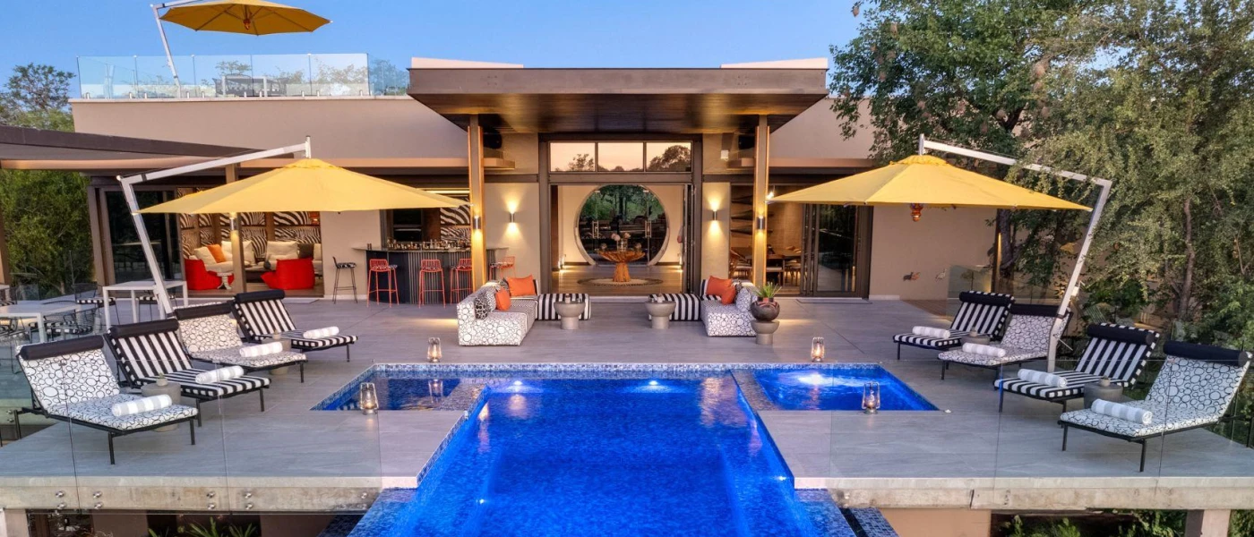 Lantern-lit swimming pool in a stone terrace with patterned loungers and yellow parasols