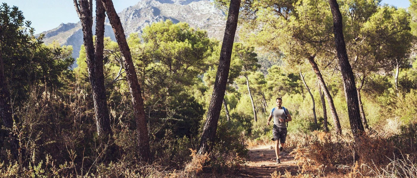 Man in active wear runs through woodland with mountains in the background