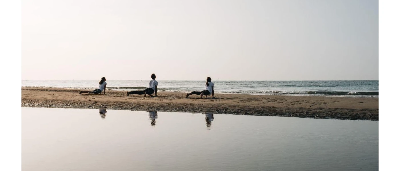 Three people in white practice yoga on the beach under a morning sky
