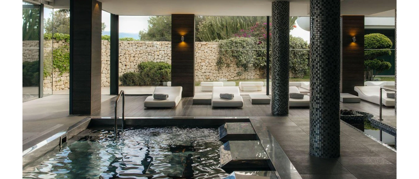 Indoor pool in a room full of pillars, with white modern daybeds and full-length windows