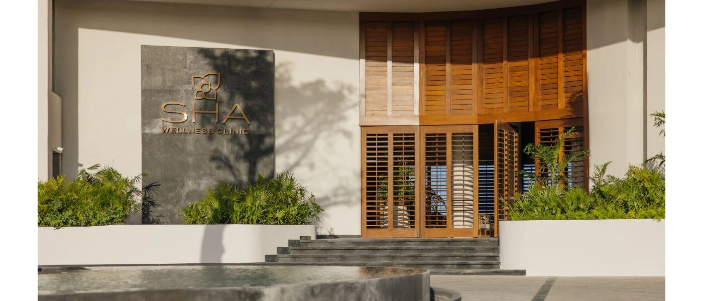 SHA Wellness Clinic entrance, with large wood-panelled doors, stone steps and palm shrubs either side
