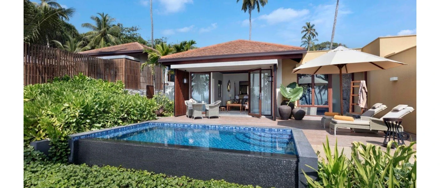 Villa with doors open to a swimming pool and terrace with loungers and umbrellas, potted plants and a table and chairs