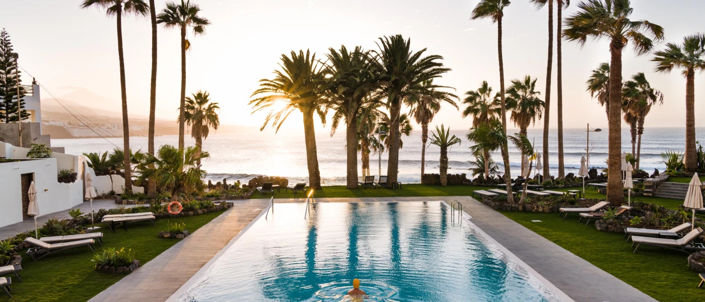 Rectangular swimming pool in a grass lawn with palm trees and loungers and a sea view