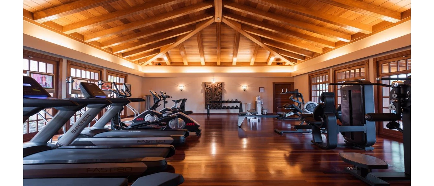 Spacious gym with a wood-beamed ceiling, wooden flooring, and black equipment including treadmills, bikes, benches and weight machines
