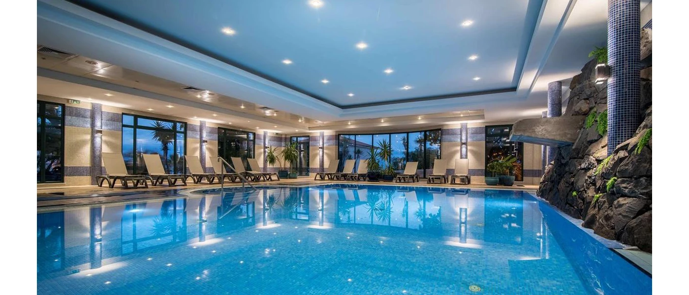 Indoor pool with a grotto-like rock wall, ceiling spotlights, and surrounding loungers