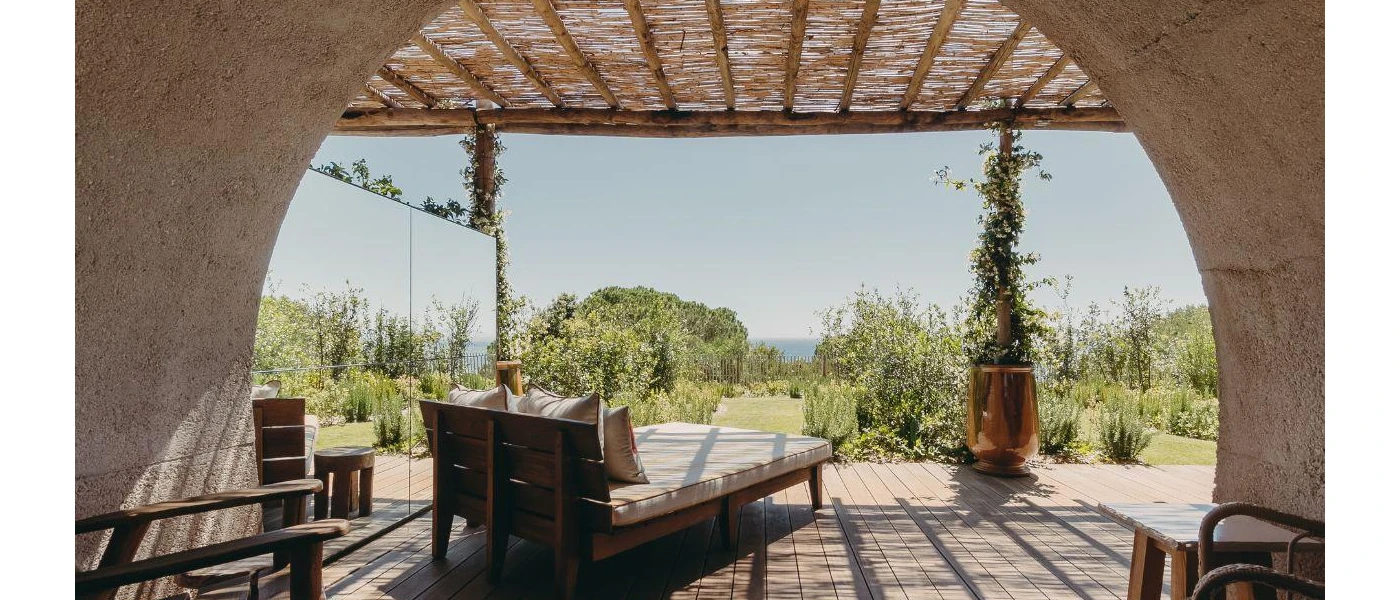 Terrace with a rattan roof, ivory-cushioned wooden loungers and views over leafy gardens