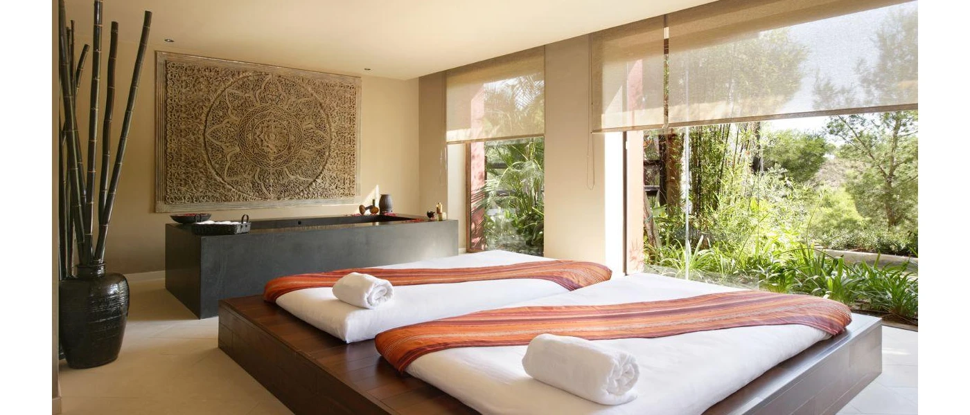 Treatment room with oversized dark-wood daybeds with white cushions next to a dark