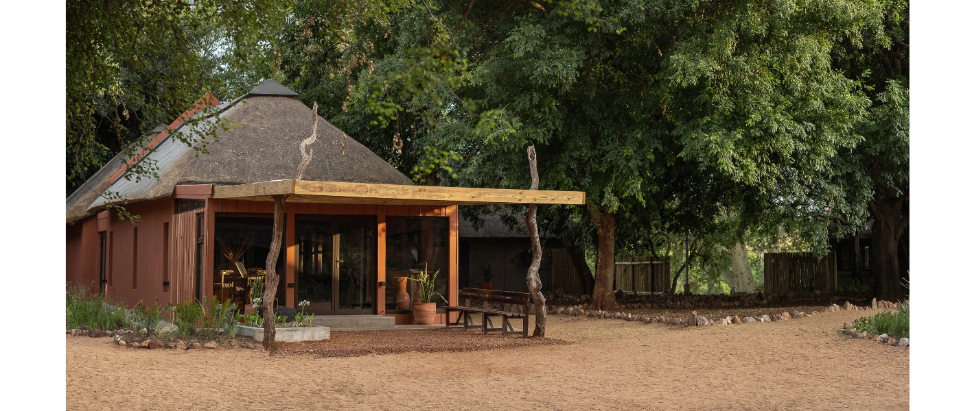 Retreat entrance with a triangular-shaped roof, wooden walls and stilts and soft lighting among thick greenery