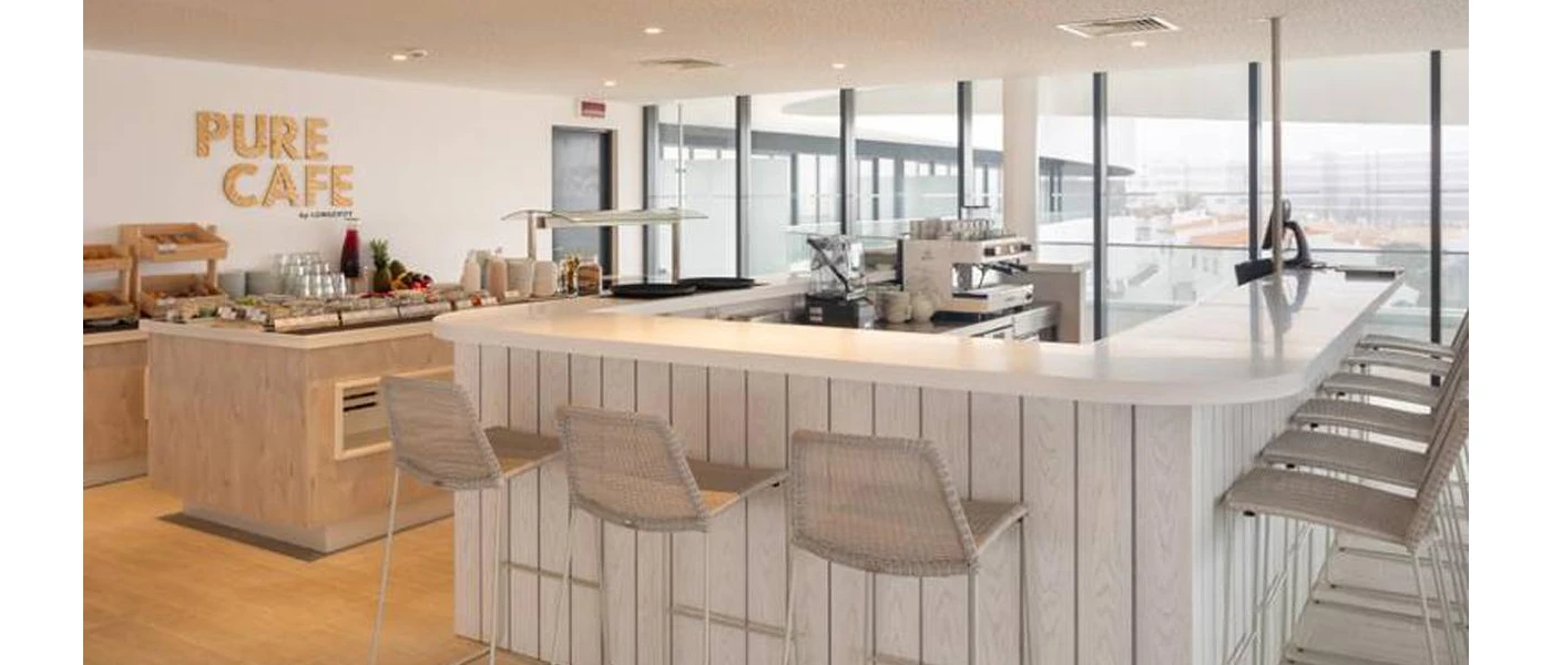Airy rooftop restaurant with a central white bar, wooden buffet stations and a sign on the wall that reads 'Pure Cafe'