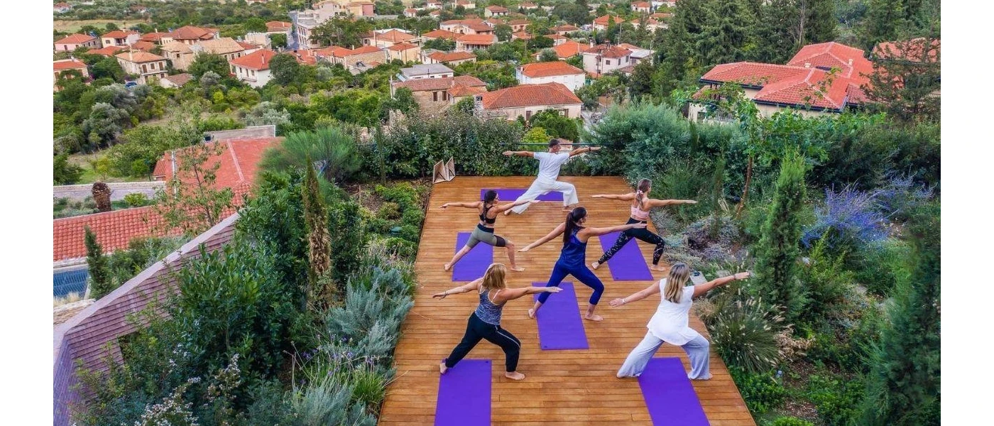 Group enjoy a class on purple yoga mats in a wood-decked garden, overlooking a sea of terracotta rooftops
