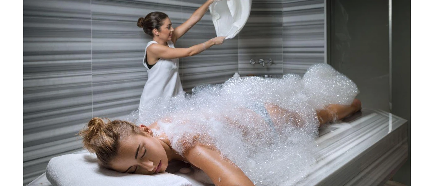 Woman lies on her front covered in foam as a therapist readies a towel behind her
