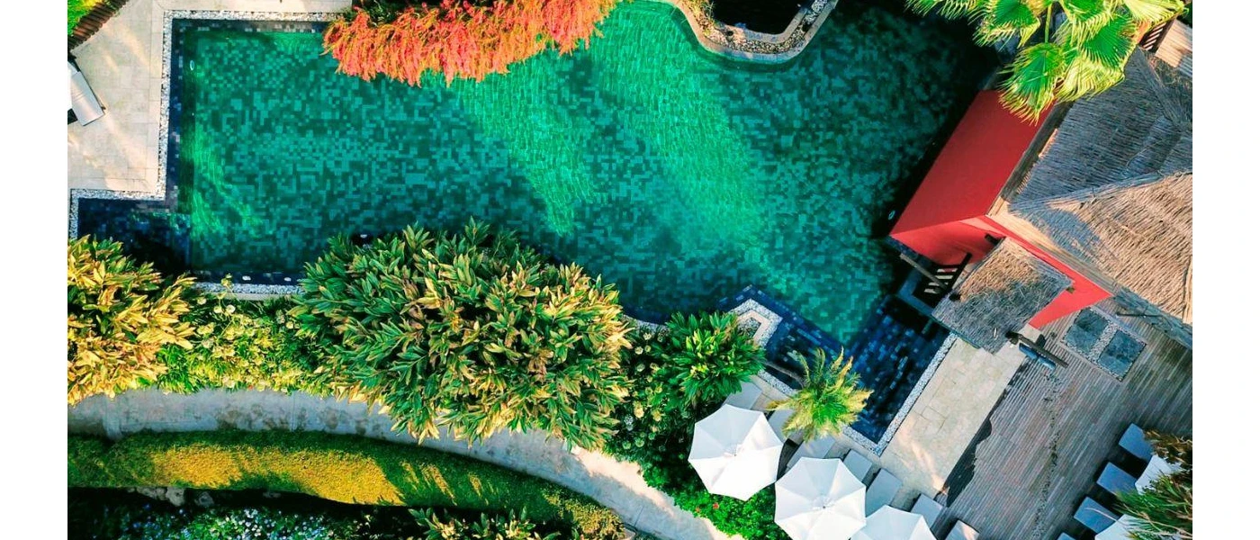 Tiled swimming pool with thatched rooftops and tropical greenery