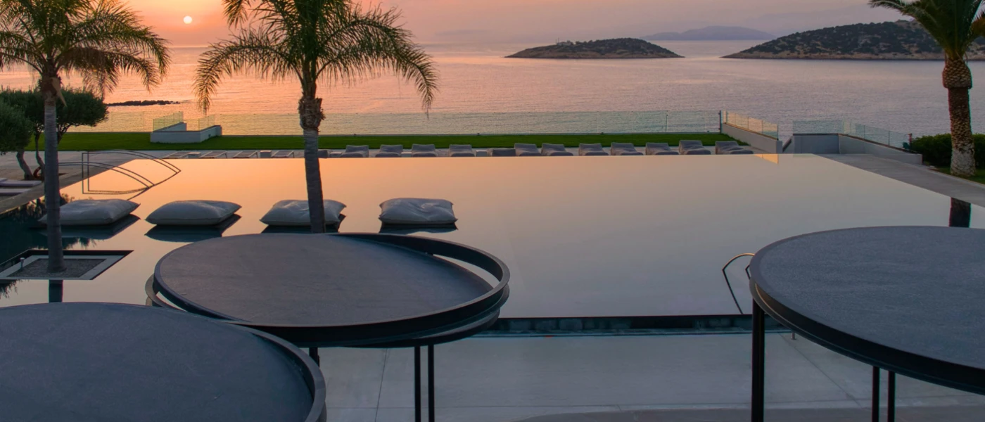 Pool terrace at sunset, with an ocean view, infinity edge and surrounding of palm trees
