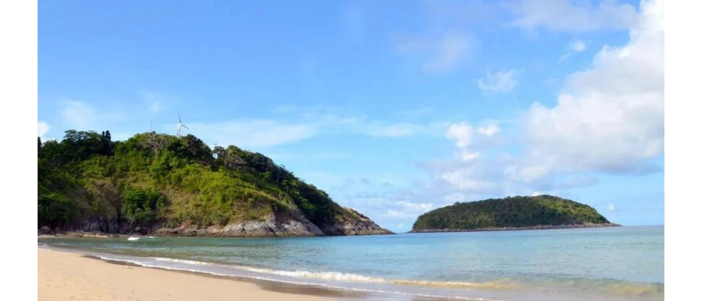 Sandy beach lapped by the ocean next to a green hillside and under a blue sky