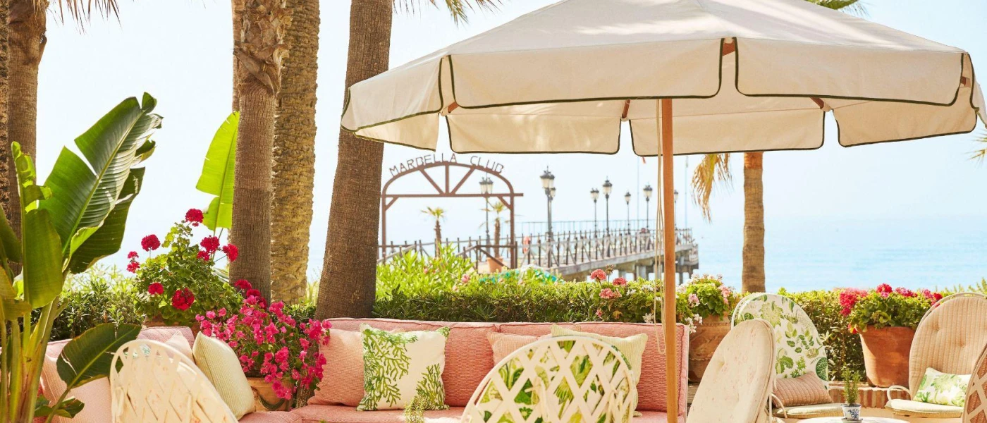 Pretty al fresco seating area, with pink sofas, green and white cushions, pink bougainvillea and palm trees and the Marbella Club-named pier in the background