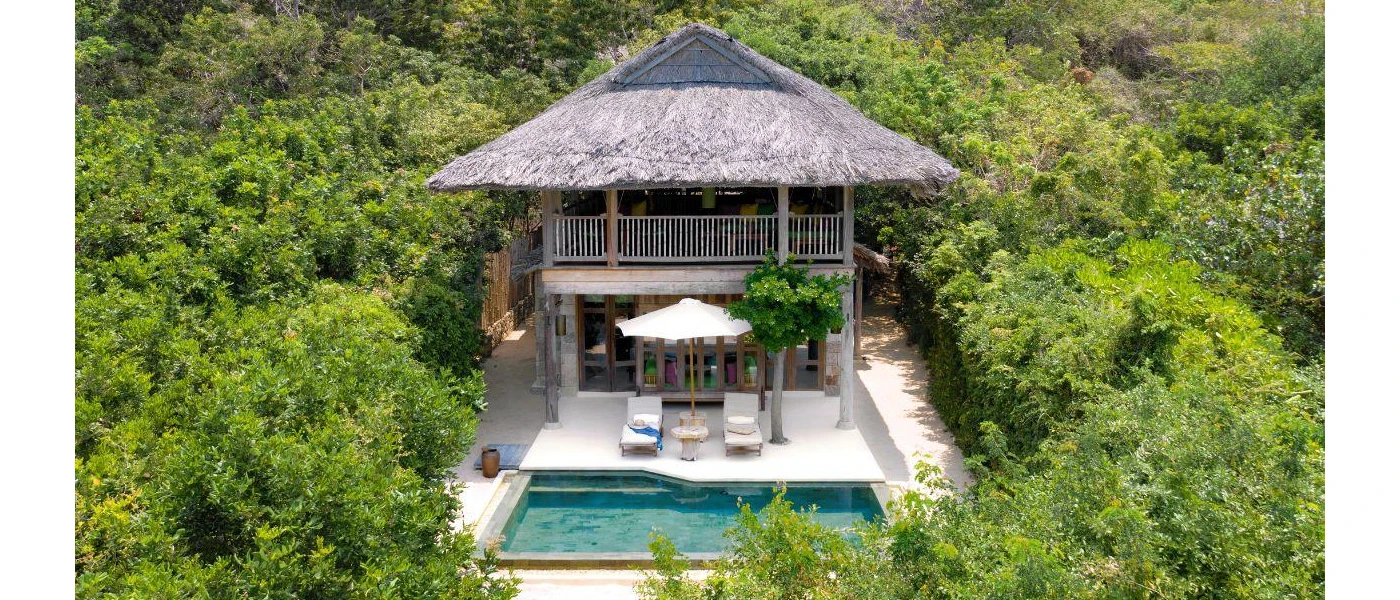 Luxury villa in a tropical forest, with a grey thatched roof, two storeys, a private pool and loungers and an umbrella 