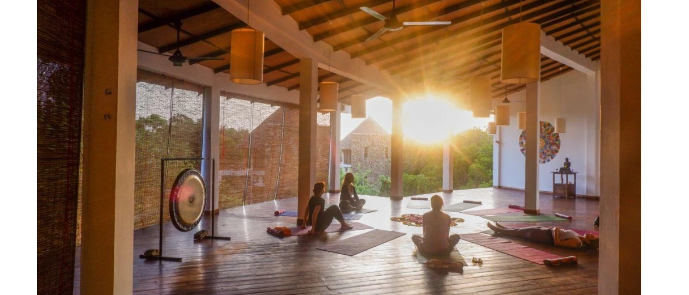 Group in a light-filled studio, with yoga mats and a large gong as the sun rises in the distance