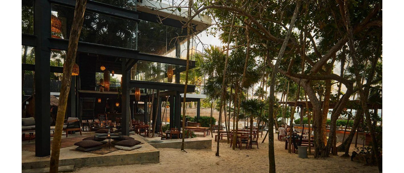 Three-storey wooden building with outdoor tables and chairs in a wooded area