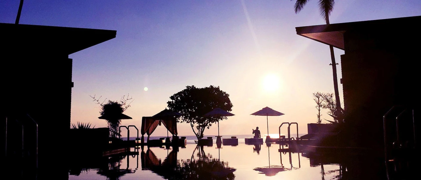 Sunset over the pool, with the silhouette of palm trees and villas