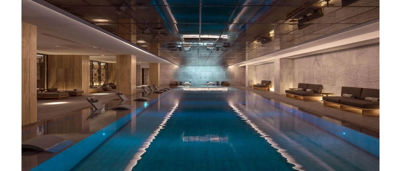 Indoor pool in a marble-walled spa area, with atmospheric lighting and cushioned loungers