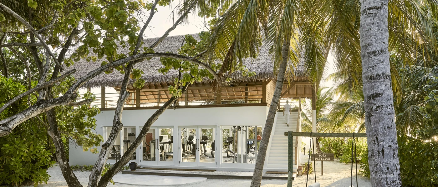 Thatched-roof, white wood panelled gym exterior, with windows showcasing the equipment inside