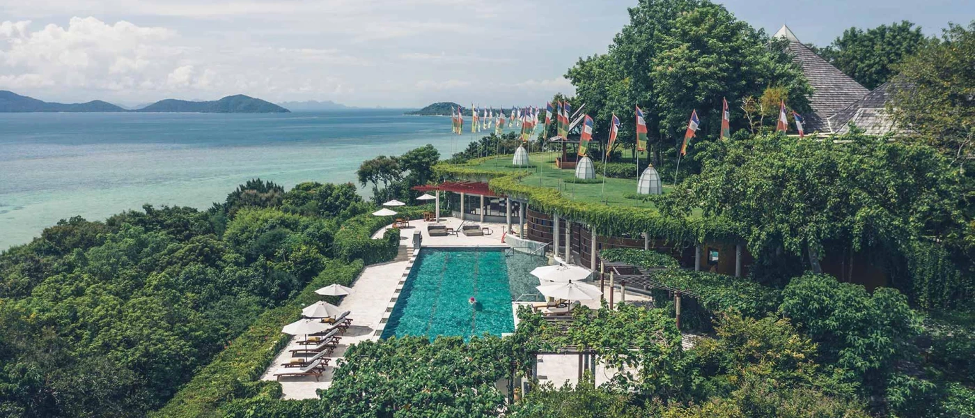 Tropical jungle setting with a terrace and swimming pool, loungers and parasols and a view of the ocean 