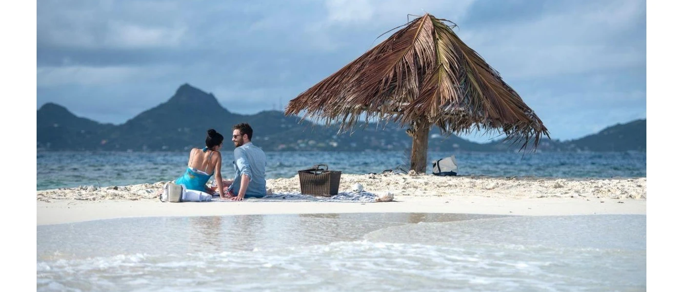 Couple hand in hand on the white sand overlooking the ocean and distant mountains