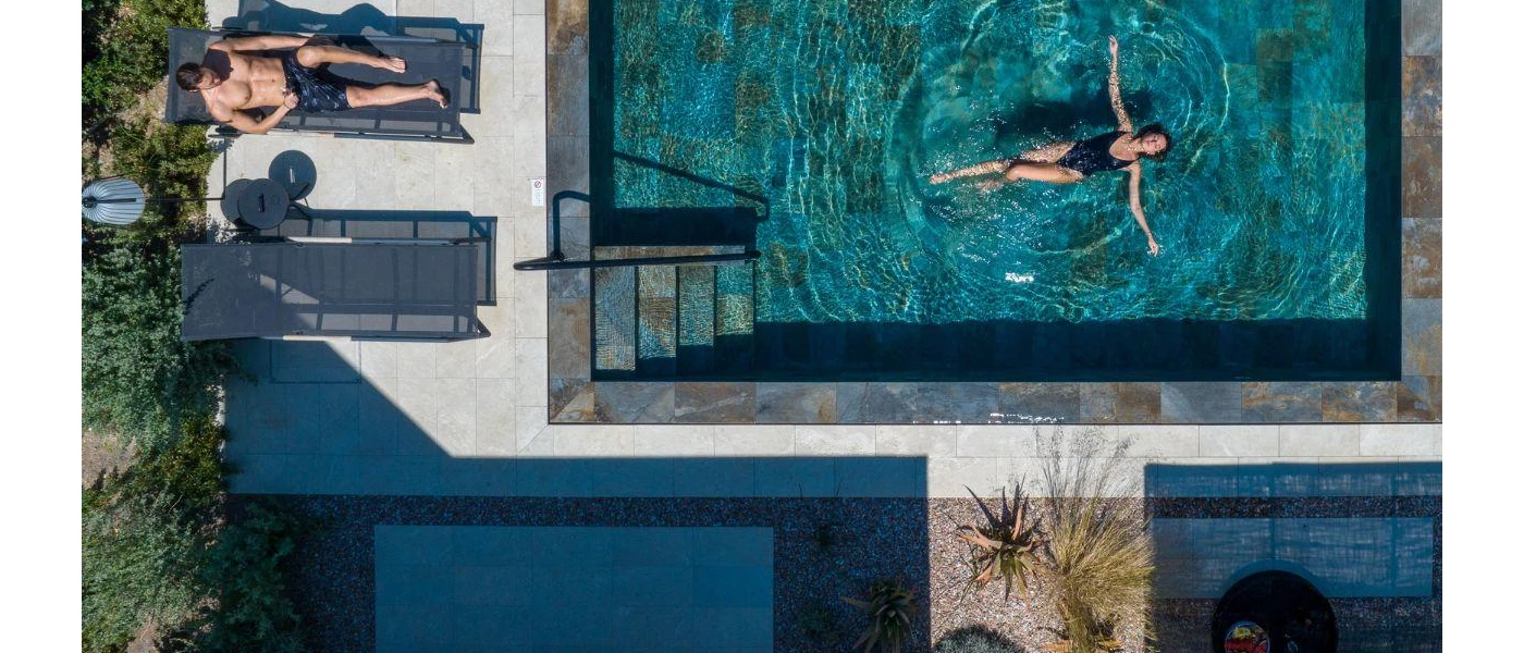 Woman relaxes on her back in a private pool, while a man lounges on the sunbed on the terrace next to it