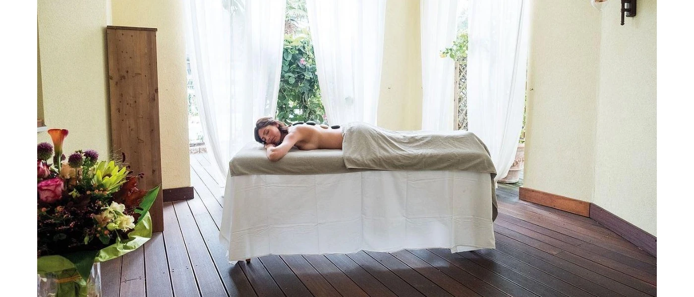 Woman lies on a massage bed half draped in a beige towel with stones on her back